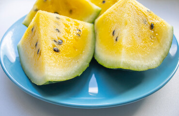 slices of watermelon with yellow pulp and seeds lie on a blue plate, on a light surface. Diet, fruits, seasonal vitamins. Yellow watermelon