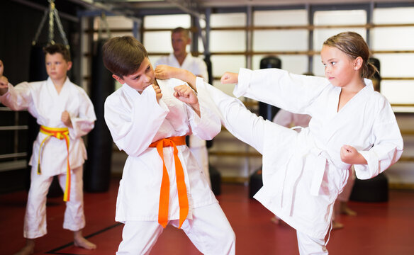 Preteen boy and girl, working in pair, mastering new karate moves in class