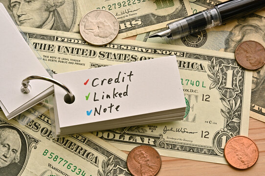 On top of the dollar bills on the table, there is a word book with the financial term credit linked note written on it.