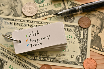On top of the dollar bills on the table, there is a word book with the financial term High Frequency Trade written on it.