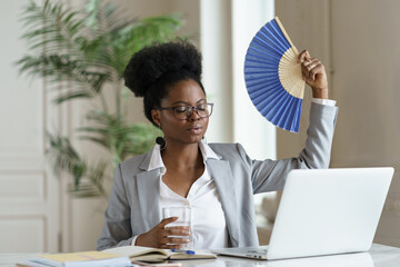 Exhausted businesswoman working tired of heat waving paper fan for fresh air. Millennial african...