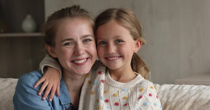 Close up portrait young attractive woman cuddling her little 9s daughter, beautiful people sit on sofa at home smiling look pose at camera. Concept of family ties and bonding, love, Happy Mother Day