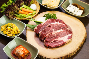 Fresh and raw expensive A5 Wagyu marble beef meat ready to grill on a wooden tray with kimchi side dish and vegetable. Traditional Korean BBQ or Japanese Yakiniku Barbecue concept. Selective focus.