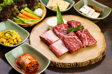Fresh and raw expensive A5 Wagyu marble beef meat ready to grill on a wooden tray with kimchi side dish and vegetable. Traditional Korean BBQ or Japanese Yakiniku Barbecue concept. Selective focus.