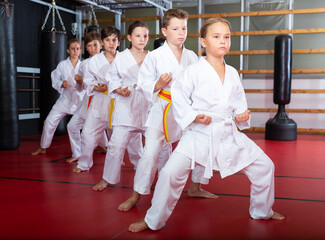 Kids in kimonos practicing effective karate techniques in group workout at training room