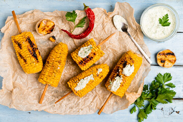 grilled corn on a blue wooden table with green sauce