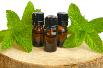 Peppermint essential oil isolated on white background.Glass bottles and sprigs of mint on a wooden saw cut close-up.Organic pure peppermint oil.Natural bio cosmetics and aromatherapy. 
