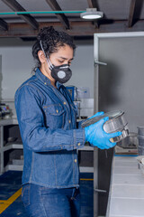Fototapeta na wymiar Female industrial worker with protective mask and blue latex gloves, holding aluminum containers for geological testing of materials
