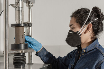 Industrial female worker with protective mask and blue latex gloves, testing a clay cylinder in...
