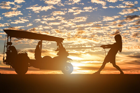 Silhouette of female pulling Motor tricycle at sunset background.