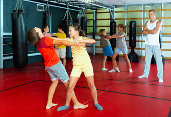 Fototapeta na wymiar Girls and boys performing self-defence moves in gym during their group training.