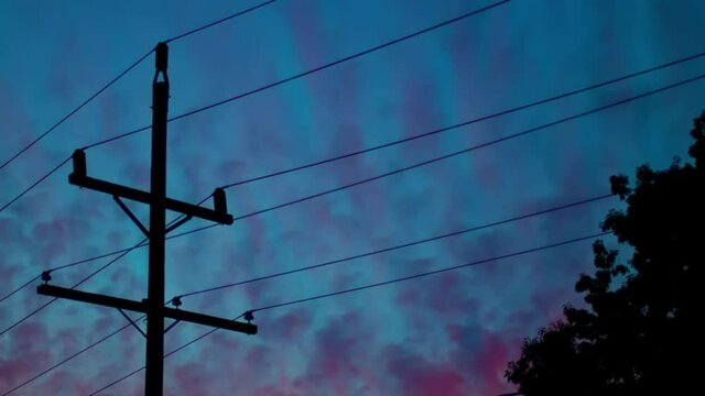 Silhouette Of Powerlines With Pink Clouds Going Past At Sunset. Timelaspe. Locked Off, Low Angle 