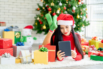 Obraz na płótnie Canvas Pretty woman lie on floor among decoration of Christmas festival and she use tablet look like for online shopping with happiness.