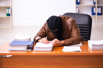 Young man in balaclava stealing information from the office