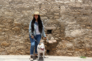 Young Latina woman with a mask accompanied by her white pitbull dog walks through the cobbled streets of a colonial-style town as a tourist
