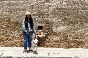 Fototapeta premium Young Latina woman with a mask accompanied by her white pitbull dog walks through the cobbled streets of a colonial-style town as a tourist 