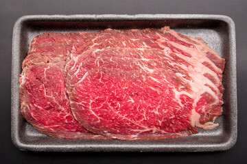 Sliced raw beef place in a row on a black plastic tray isolated on a black background. Sliced ​​meat for cooking, fresh meat for grilling, yakiniku, sukiyaki or shabu.