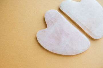 face massage scraper made of rose quartz close-up on a clean beige background. cosmetic layout. home facial care. selective focus