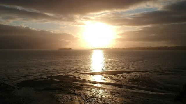 Drone footage flying towards the sunrise - Howick, east Auckland in New Zealand. Cloudy Skies with the sun breaking through with its golden beams shining down on the bays below.