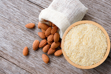 Almond flour in wooden bowl and almonds nut isolated on wooden table background. Top view. Flat lay.
