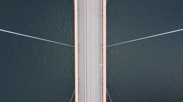 Mighty Cables holding suspension bridge Hardangerbrua - Forward moving birseye aerial over bridge with cables passing close - Hardangerfjorden sea below - Norway