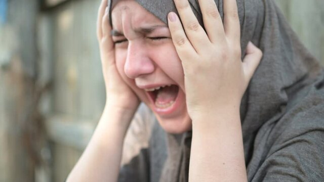 a teenage refugee girl is crying and screaming, holding her head in her hands, screaming in pain.
