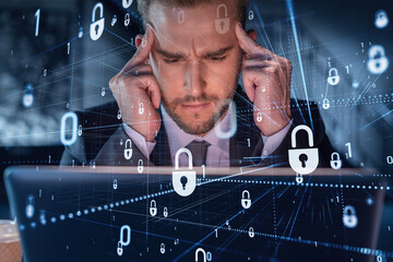 Handsome businessman in suit at workplace working with laptop to defend customer cyber security. Concept of clients information protection and brainstorm. Padlock hologram over office background.