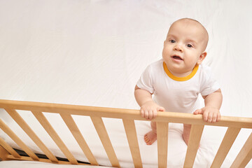 Cute small boy at house. Childhood concept. Light background. Smiling child. Happy emotion. Copyspace. Stay home. Onesie mockup. White clothes. Stay near bed