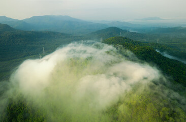 Aerial view Transmission tower in green forest and beautiful morning smooth fog. Energy and environment concept. High voltage power poles. Pang Puay, Mae Moh, Lampang, Thailand.