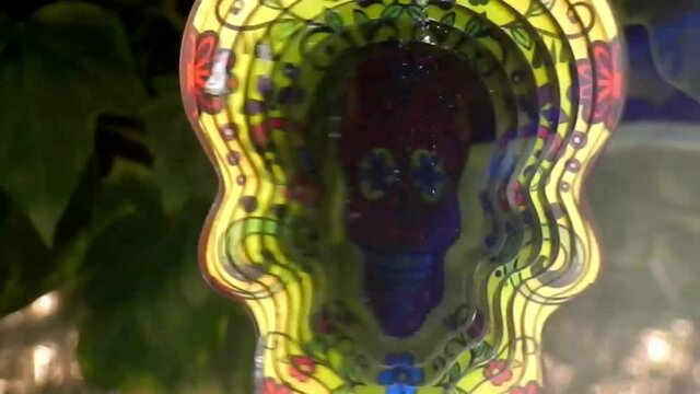 Hypnotic metal sugar skull decorative colourful spinning garden ornament hanging from tree closeup shot