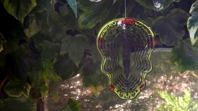 Hypnotic metal sugar skull decorative colourful spinning garden ornament hanging from tree closeup