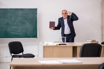 Old male teacher in front of blackboard
