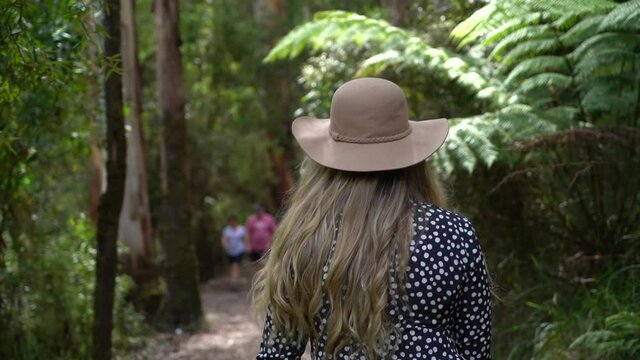 Blonde woman explore dense jungle forest while wearing hat, back follow up view