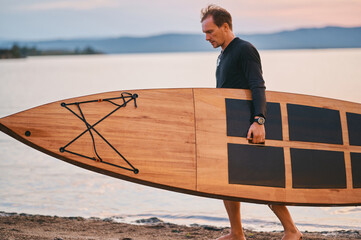 Man carrying wooden surf board in hand
