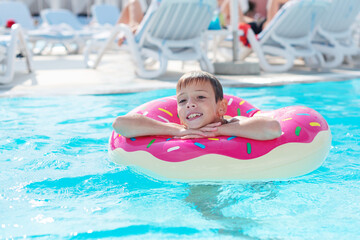 Fototapeta premium Happy little boy with variegated life ring in the form of a donut has fun in the swimming pool