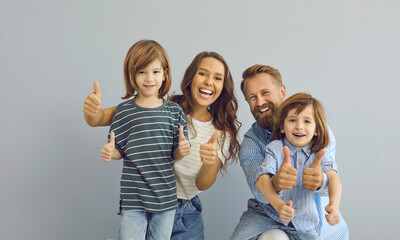 Studio shot of happy Caucasian family of four. Cheerful mother, father and children giving thumbs...