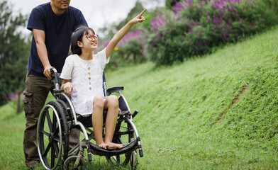 Obraz premium Father and Disabled child on wheelchair walking on trail meadow park in sunny day. Happy disability kid travel in family holiday concept.