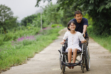 Father and Disabled child on wheelchair walking on trail park in sunny day. Happy disability kid travel in family holiday concept. - obrazy, fototapety, plakaty