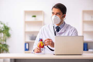 Young male doctor cardiologist working in the clinic during pand