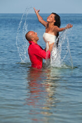 Fototapeta premium Romantic newly-married couple enjoying a summer vacation. Young groom lifting his bride in sea