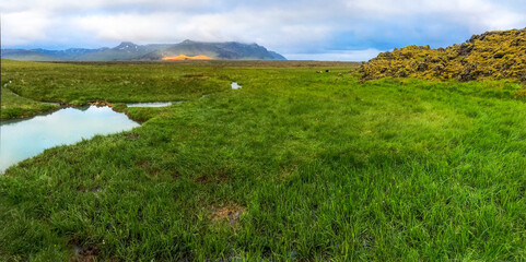 Hot geothermal springs among green moss against backdrop of yellow mountains