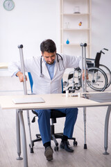 Young male doctor with crutches working in the clinic