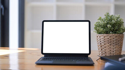 Mock up computer tablet with white display, houseplant and notebook on wooden desk.