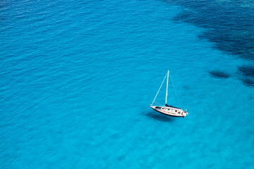 View from above, stunning aerial view of a sailboat floating on a turquoise, crystal clear water during a sunny day. Costa Smeralda, Sardinia, Italy.