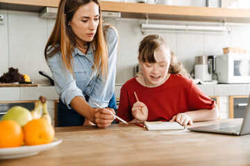 White woman helping her daughter with down syndrome doing homework
