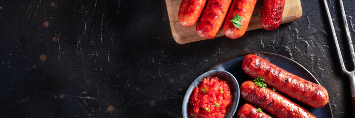 Sausages panoramic banner with a place for text, top shot on a black slate background