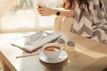 Cup of coffee and cupcakes on table in room
