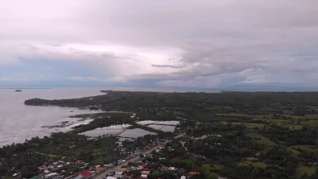 Aerial drone shot of Daanbantayan Cebu. Visible vast land area and beautiful shores. Land covered with greens, trees, rice fields and fish ponds. The sky is covered with clouds with some blues.