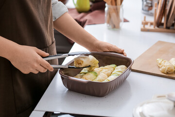 Woman preparing tasty stuffed cabbage rolls in kitchen, closeup