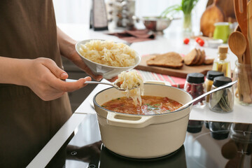 Woman preparing tasty sauerkraut soup on electric stove in kitchen, closeup
